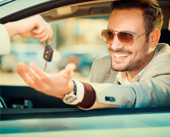Man sitting in a car reaching for car keys that are dangled in front of him.