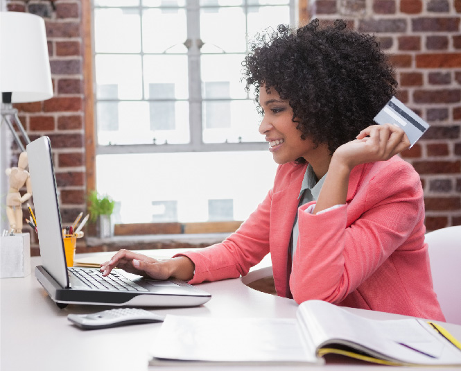 A young woman at a laptop holding a credit card and smiling.