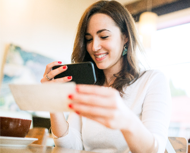 A young woman holding a check with her phone in the other hand to take a picture.